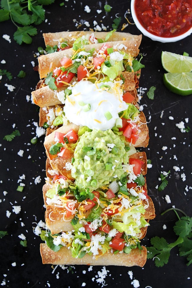 Baked Chicken Taquitos with cheese, lettuce, diced tomatoes, cilantro, sour cream, and guacamole on sheet pan. 