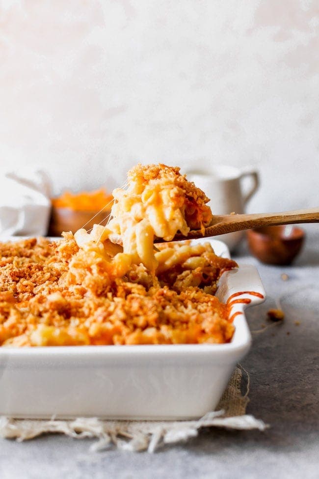 a wooden spoon scooping mac and cheese out of a baking dish. 