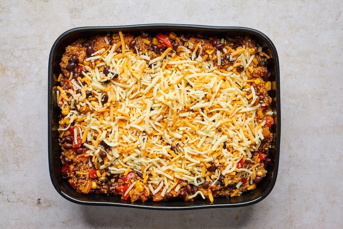 black bean quinoa enchilada bake in pan topped with shredded cheese.