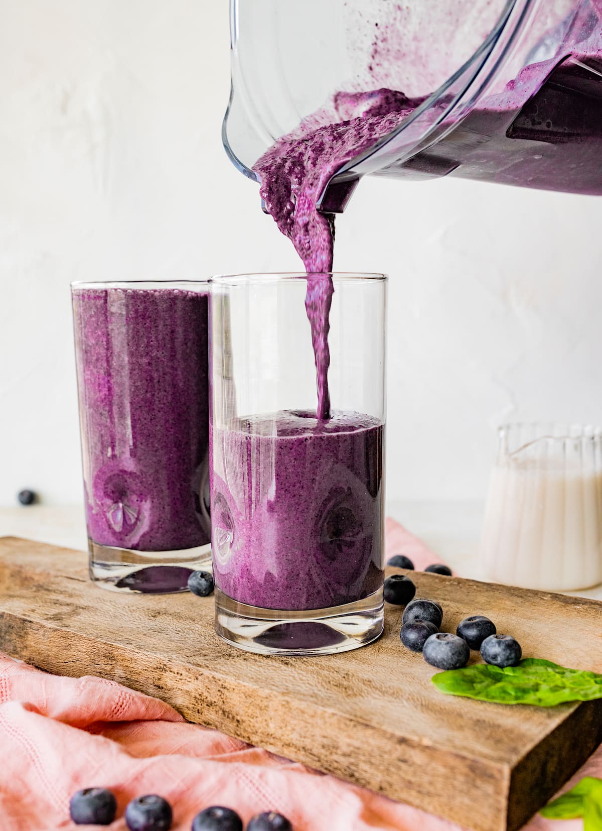 blueberry smoothie being poured into 2 glasses. 