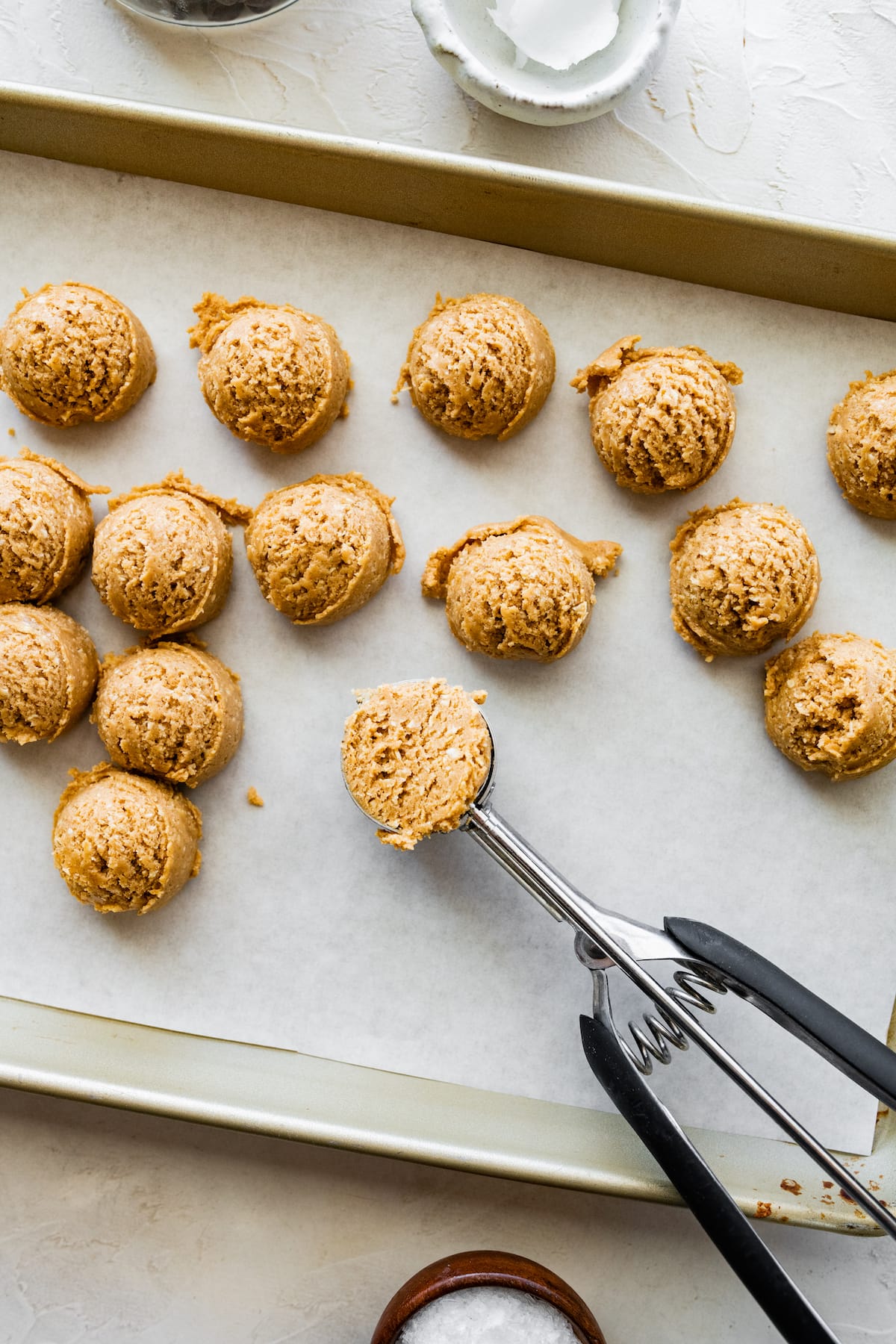 peanut butter protein balls being scooped with cookie scoop on baking sheet with parchment paper. 