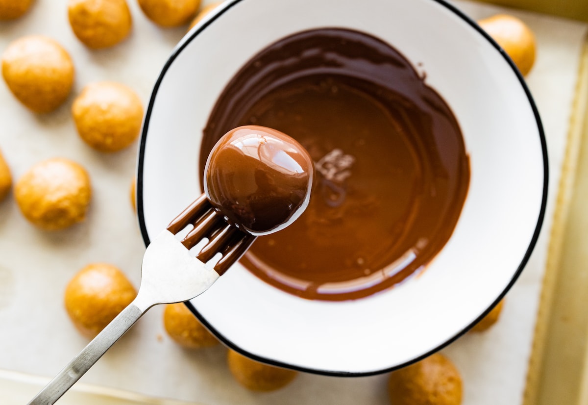 peanut butter protein balls being dunked in melted chocolate with fork. 