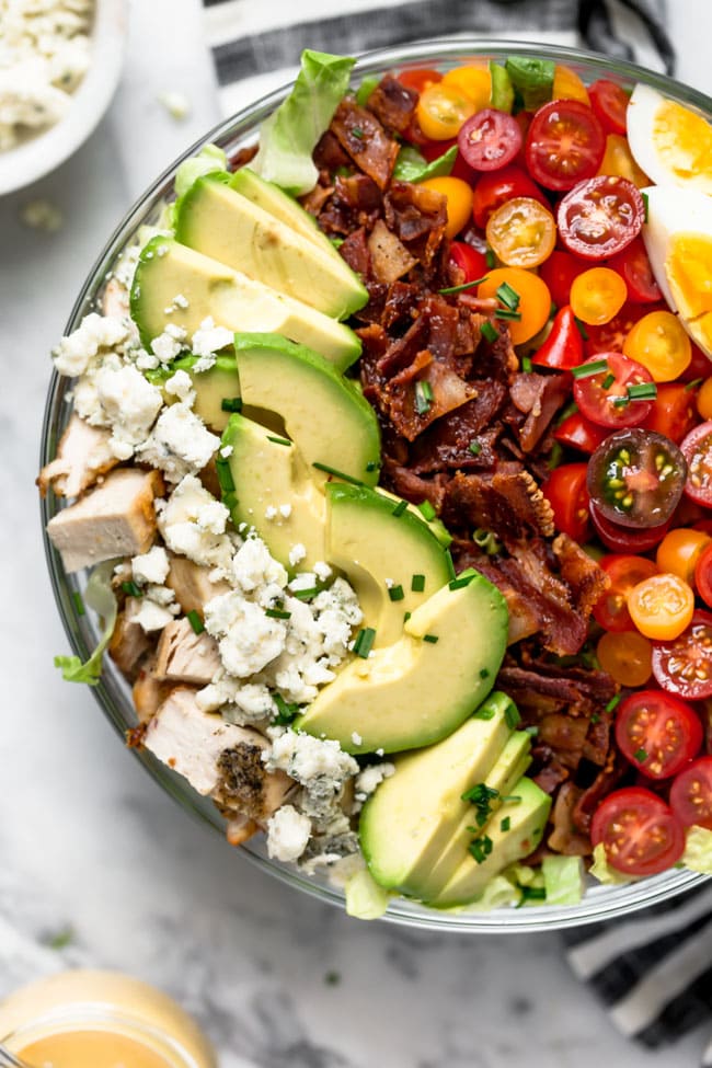 Easy Cobb Salad with chicken, bacon, avocado, cheese, tomatoes, and chives in large bowl.