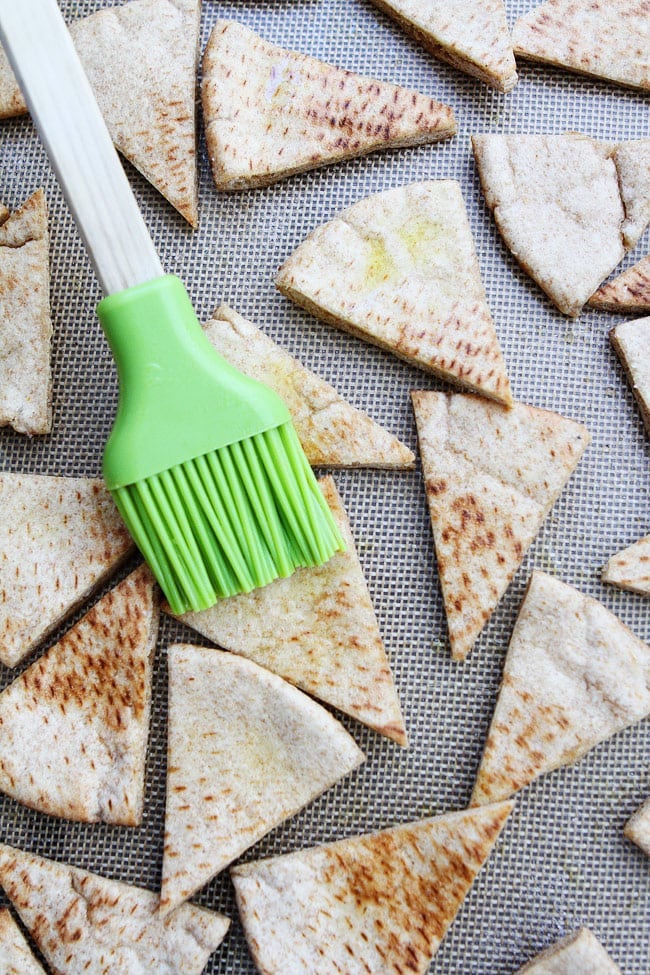 pita chips being brushed with olive oil on baking sheet. 