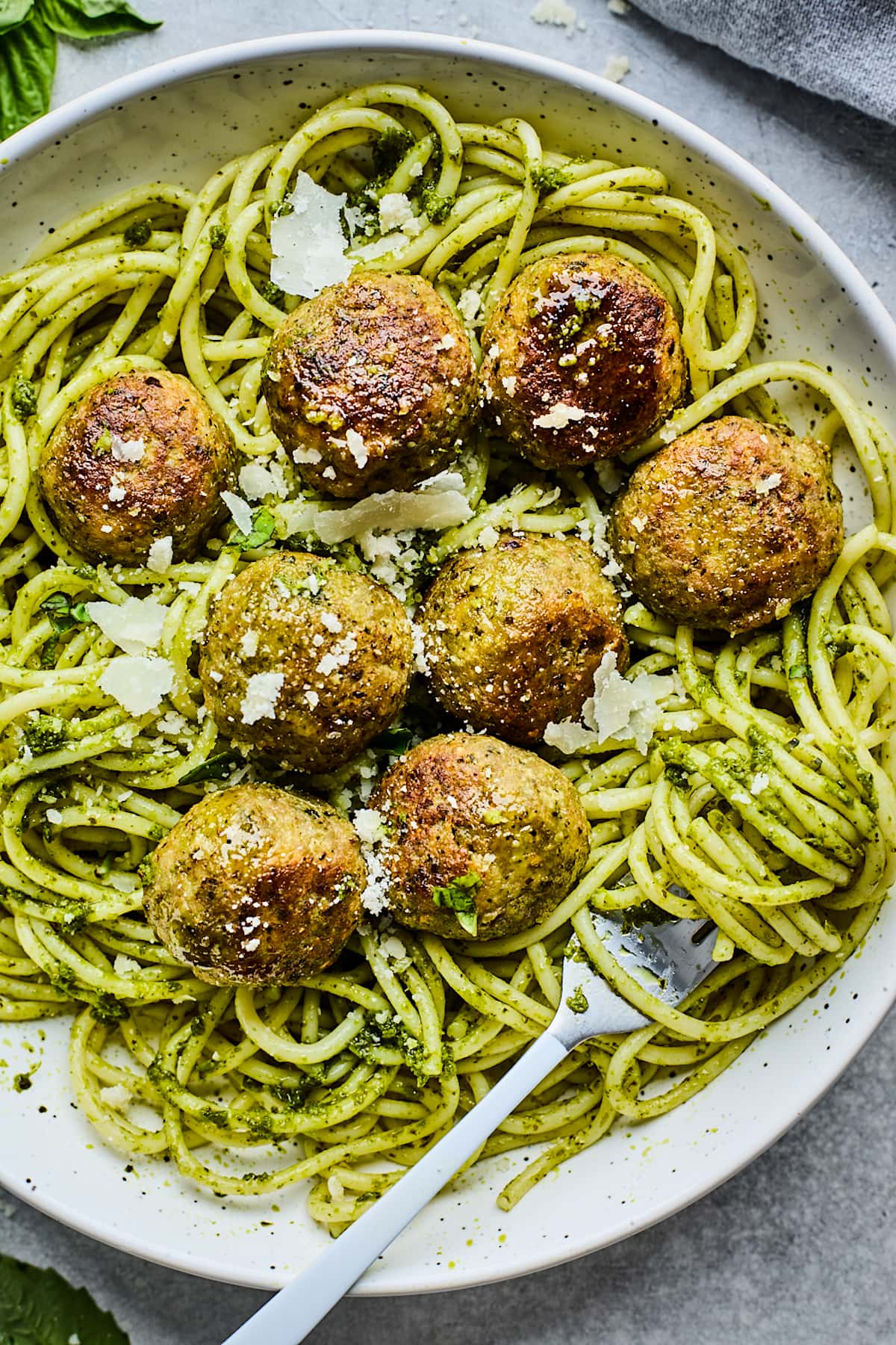 pesto meatballs with spaghetti and parmesan cheese in bowl with fork. 