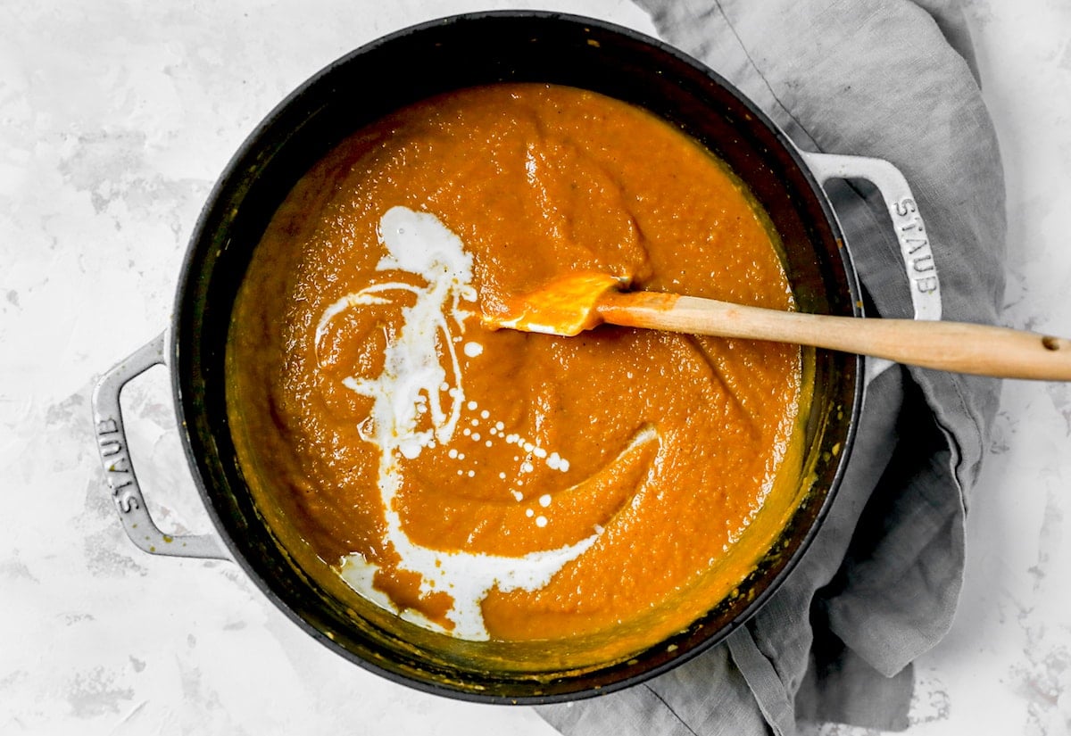 Pumpkin soup in pot with cream and spatula. 