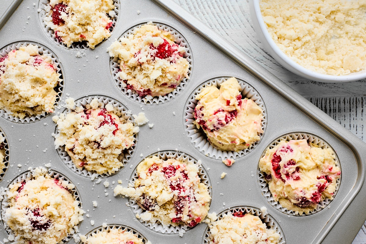 raspberry muffins in muffin pan with streusel topping ready to be baked. 