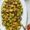 A white oval tray full of roasted brussels sprouts, with a serving spoon in it