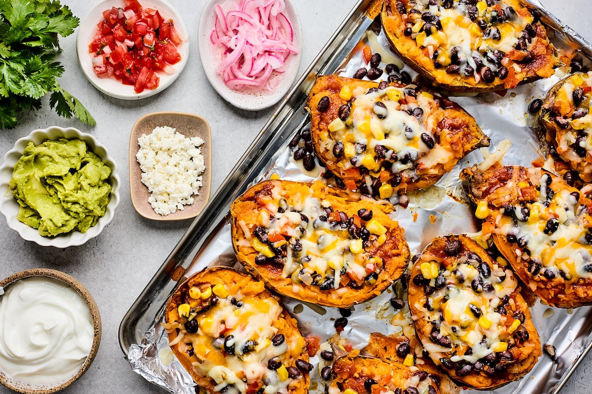 enchilada baked sweet potatoes on baking sheet with toppings. 