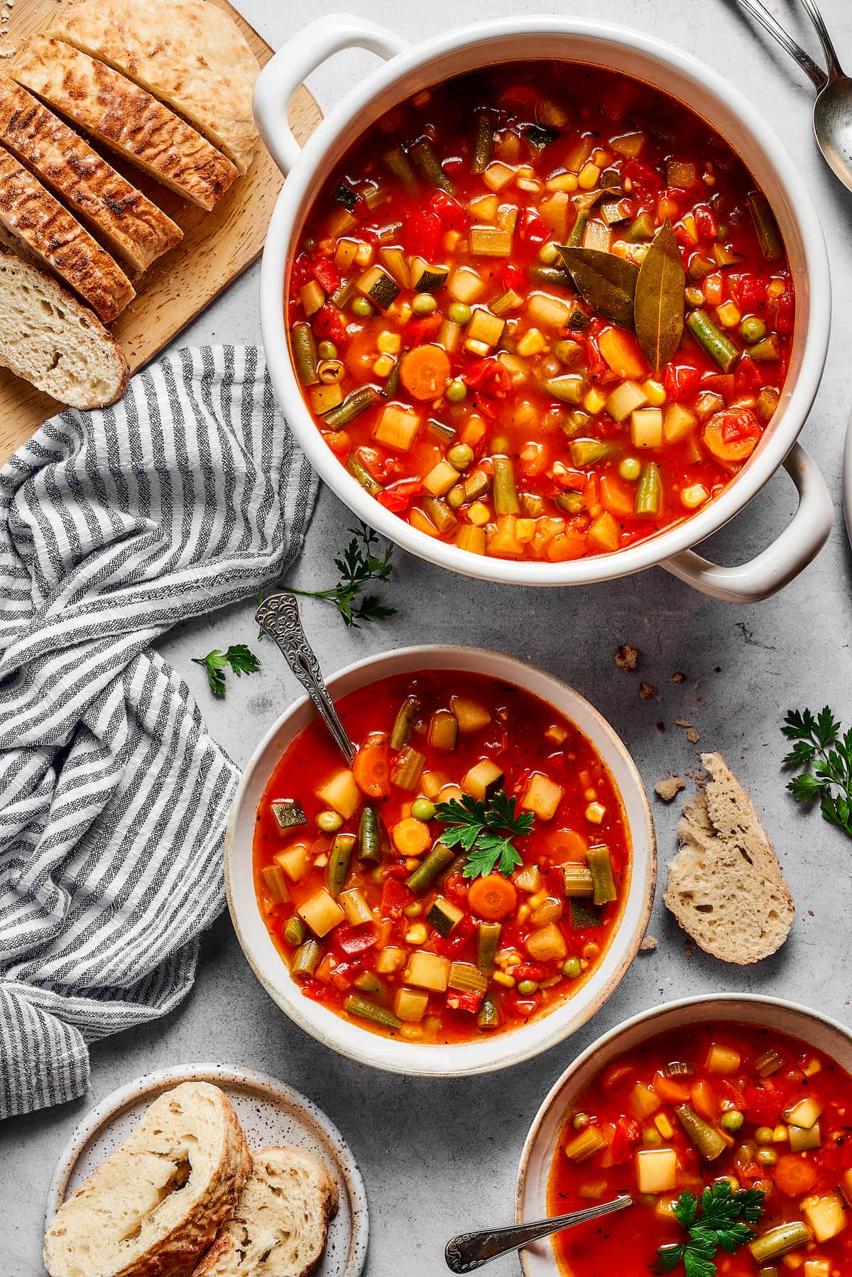 A full spread of homemade vegetable soup in two bowls, next to a large pot and a loaf of crusty bread.