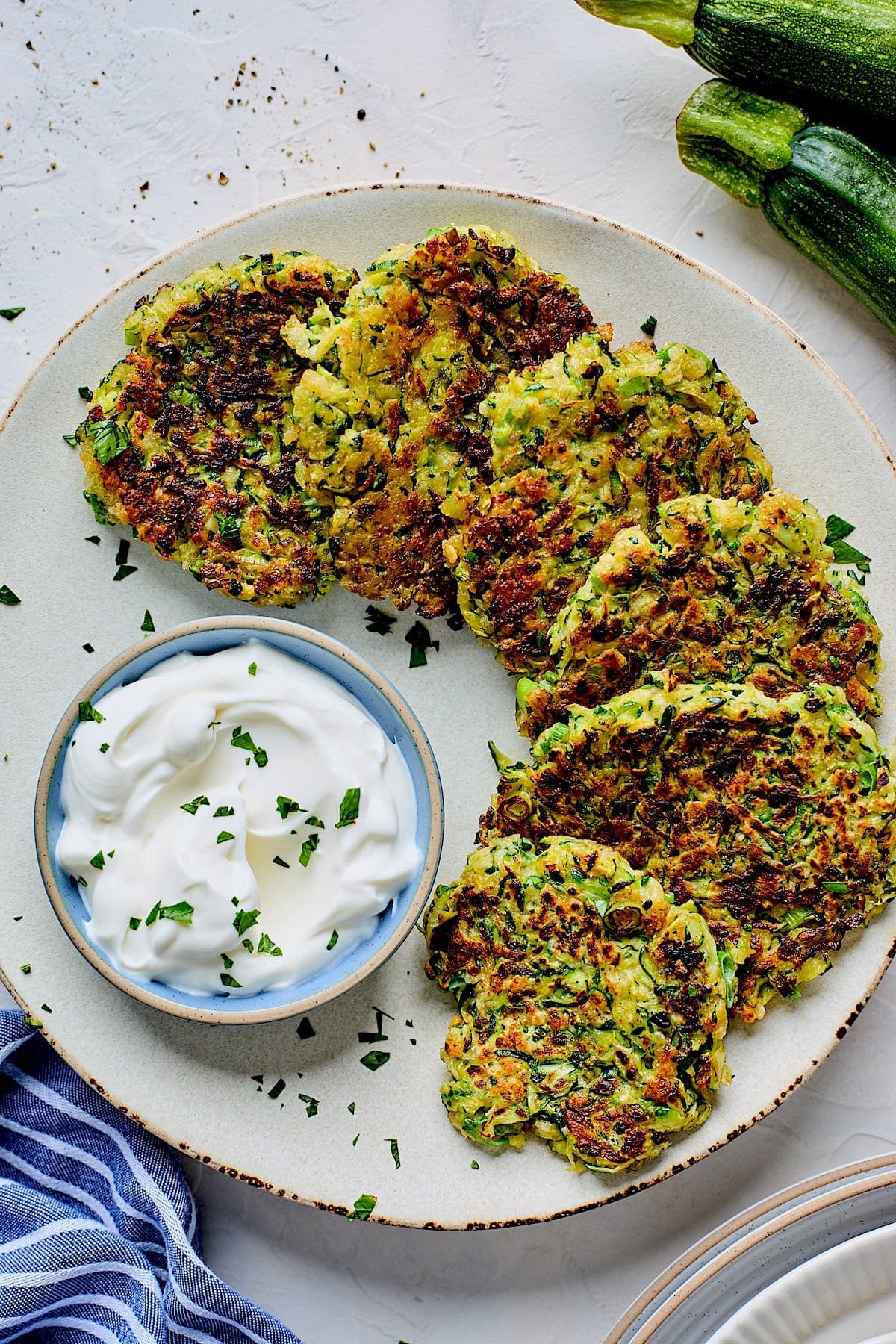zucchini fritters on plate with sour cream and herbs.